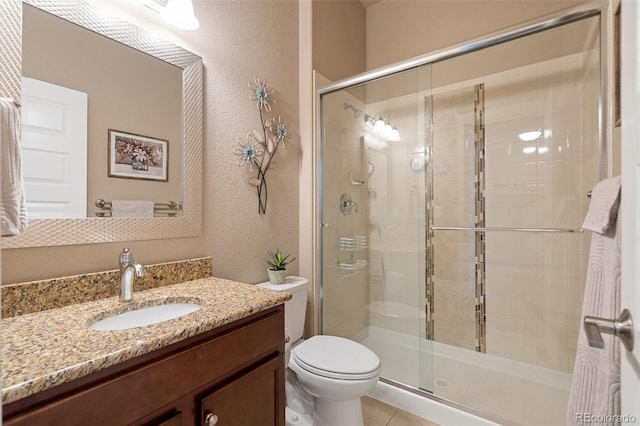 bathroom featuring a stall shower, a textured wall, toilet, tile patterned floors, and vanity