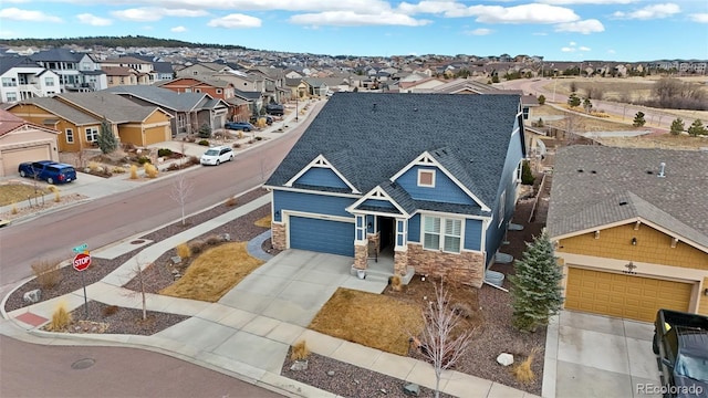 exterior space with driveway, a garage, stone siding, a residential view, and roof with shingles