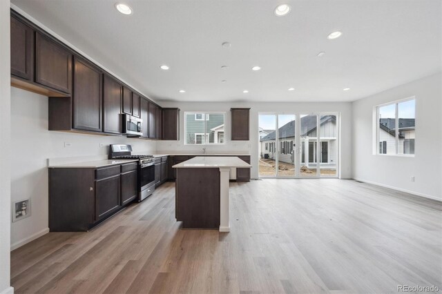 6625 N Nepal St, Aurora, CO 80019 - kitchen with dark brown cabinetry, a center island, light wood-type flooring, stainless steel appliances, and plenty of natural light