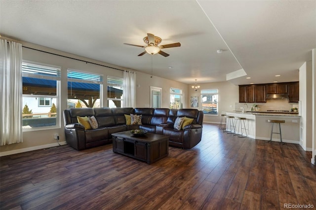 living room with dark wood-style floors, baseboards, and ceiling fan with notable chandelier