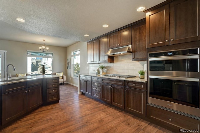 kitchen with stainless steel appliances, a sink, under cabinet range hood, and dark brown cabinetry