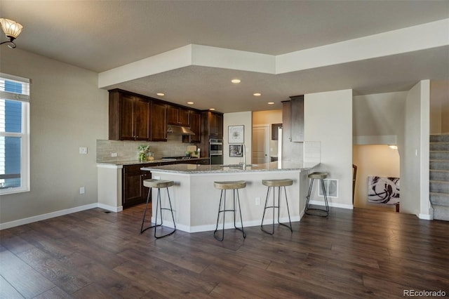 kitchen with a kitchen breakfast bar, dark wood-type flooring, backsplash, and kitchen peninsula