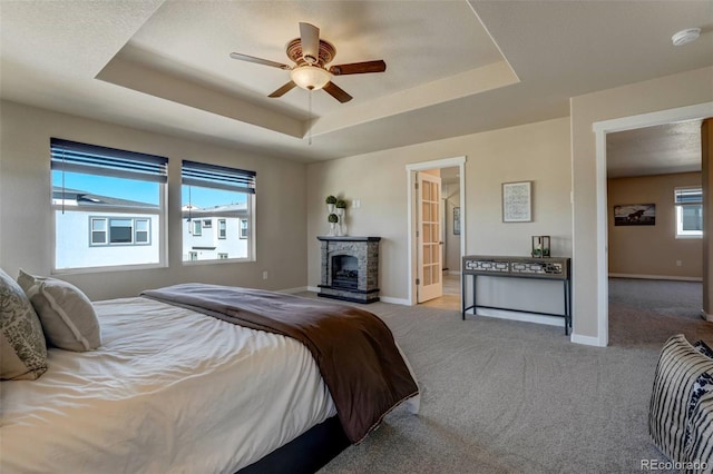 bedroom with light carpet, ceiling fan, a tray ceiling, ensuite bath, and a fireplace