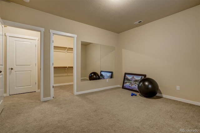 workout area with light colored carpet, visible vents, a textured ceiling, and baseboards