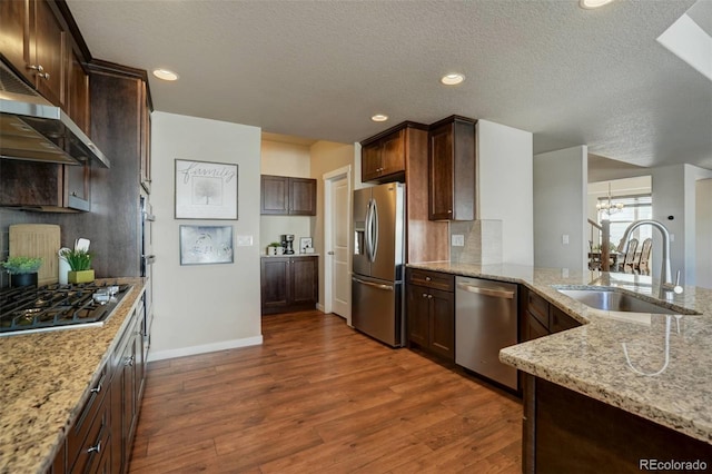 kitchen with dark wood finished floors, a notable chandelier, stainless steel appliances, a sink, and light stone countertops