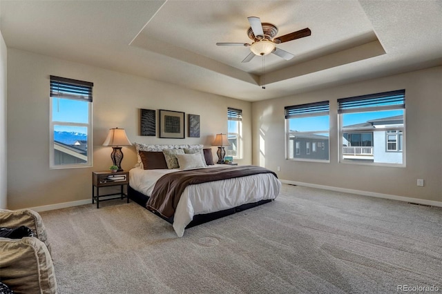 bedroom featuring ceiling fan, a tray ceiling, light colored carpet, and baseboards