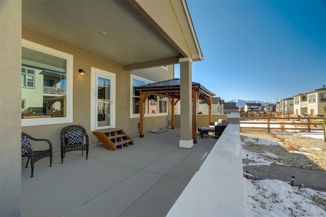 snow covered patio with a residential view, fence, and a gazebo