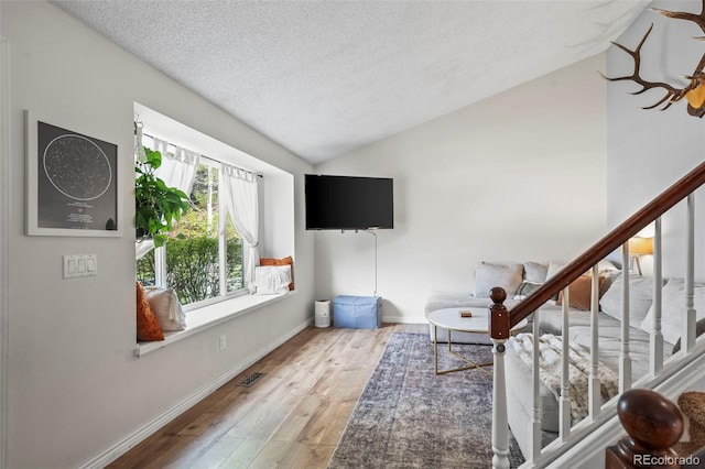 living room featuring a textured ceiling, baseboards, wood-type flooring, lofted ceiling, and visible vents
