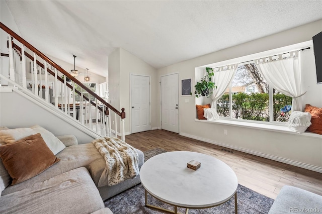 living room featuring baseboards, visible vents, lofted ceiling, wood finished floors, and stairs