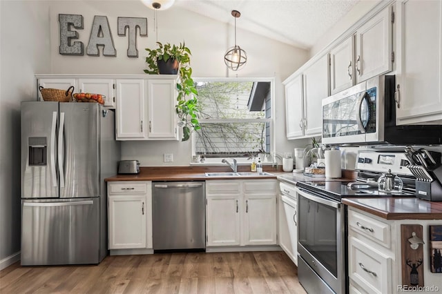 kitchen featuring butcher block counters, vaulted ceiling, stainless steel appliances, and a sink