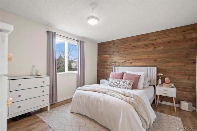 bedroom with light wood-style flooring, wood walls, and a textured ceiling