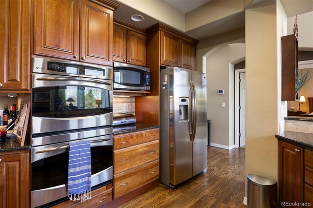 4373 E Phillips Pl, Centennial, CO 80122 - kitchen featuring dark wood-style floors, brown cabinets, arched walkways, appliances with stainless steel finishes, and backsplash