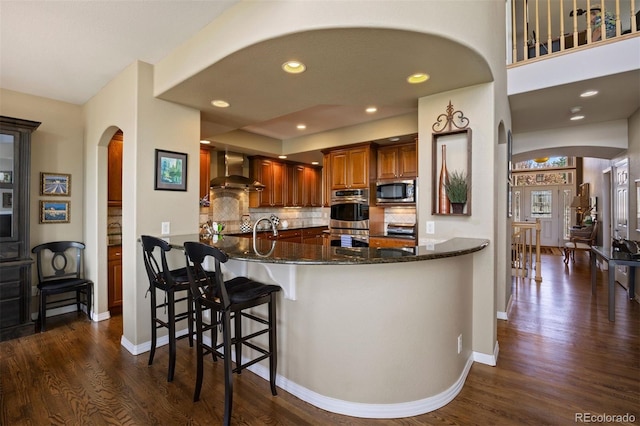 4373 E Phillips Pl, Centennial, CO 80122 - kitchen featuring dark wood-style flooring, wall chimney exhaust hood, arched walkways, dark stone countertops, and appliances with stainless steel finishes