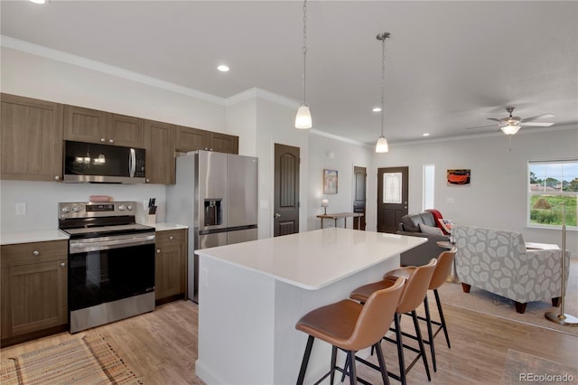 6986 Marshbern Ct, Colorado Springs, CO 80908 - kitchen featuring stainless steel appliances, light wood finished floors, a kitchen bar, a kitchen island, and ornamental molding