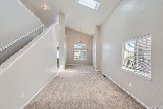 unfurnished living room featuring a skylight, lofted ceiling, carpet floors, and baseboards
