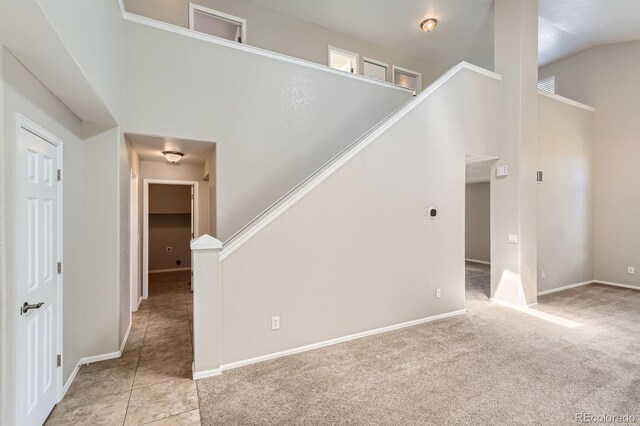 unfurnished living room featuring light colored carpet, baseboards, stairway, and vaulted ceiling