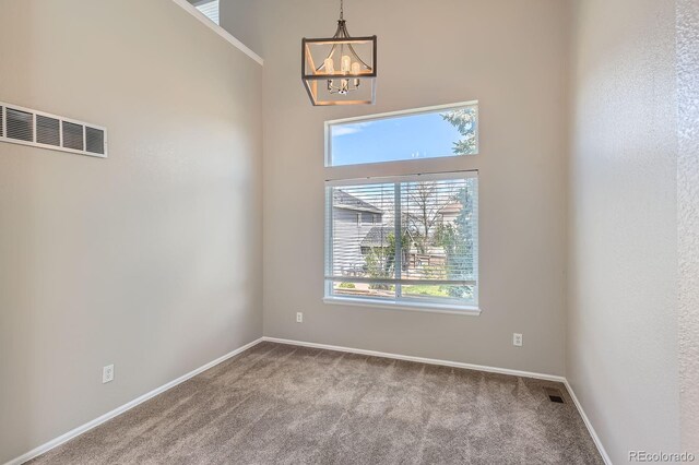 carpeted spare room with plenty of natural light, a chandelier, and baseboards