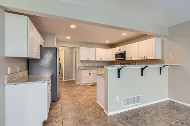 kitchen featuring appliances with stainless steel finishes, a kitchen bar, white cabinets, a peninsula, and light stone counters