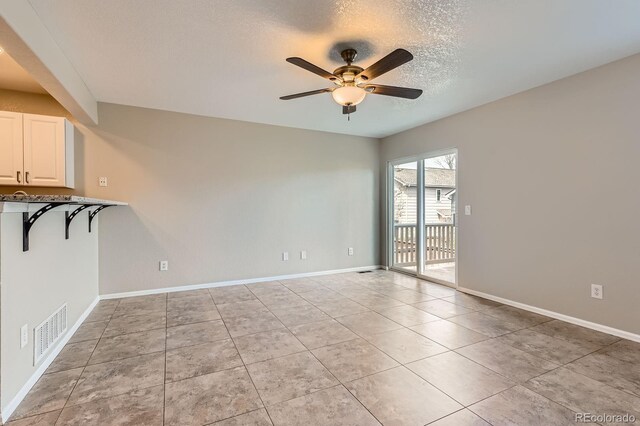 unfurnished room with a ceiling fan, light tile patterned floors, baseboards, and a textured ceiling