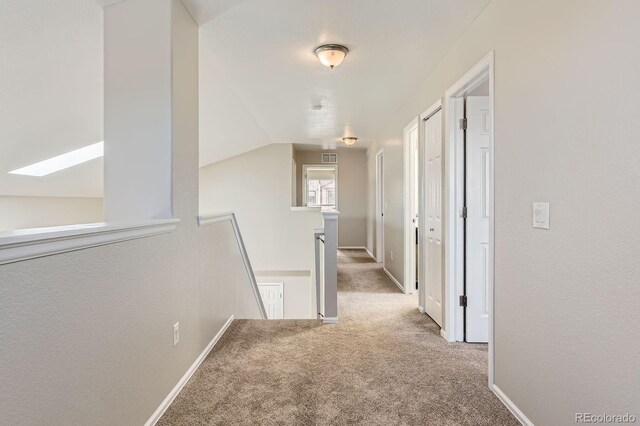 hall featuring an upstairs landing, carpet flooring, a skylight, vaulted ceiling, and baseboards