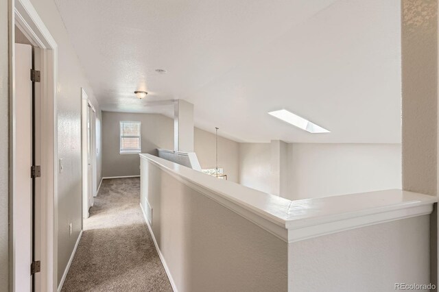 hall with a skylight, light carpet, vaulted ceiling, baseboards, and an upstairs landing