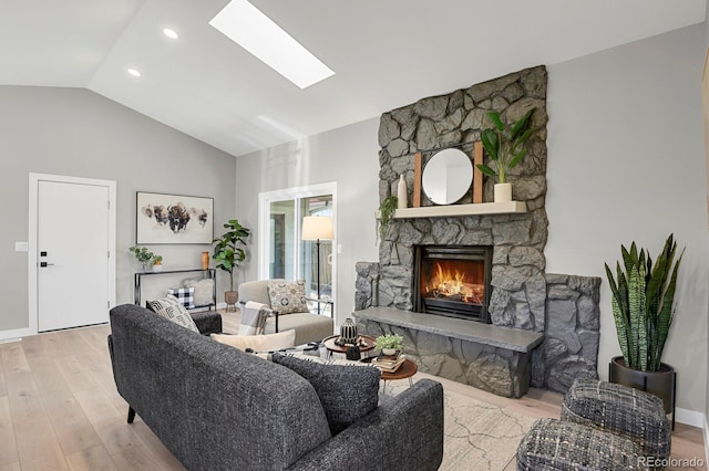 living room featuring a fireplace, light hardwood / wood-style floors, and vaulted ceiling with skylight