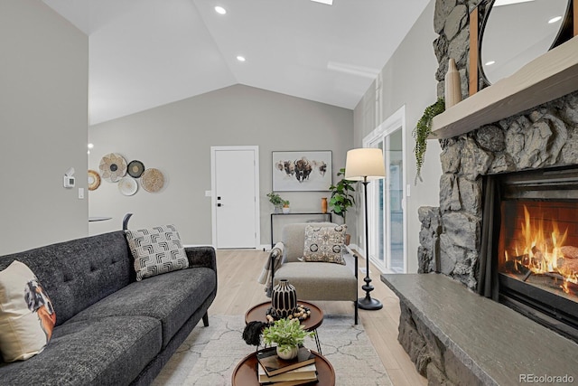 living room featuring a stone fireplace, vaulted ceiling, and light hardwood / wood-style flooring