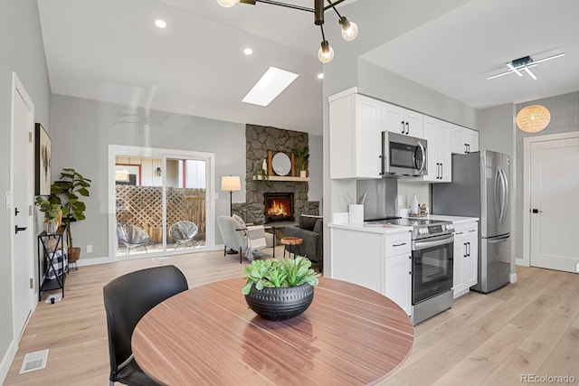 kitchen featuring lofted ceiling, light hardwood / wood-style flooring, appliances with stainless steel finishes, white cabinetry, and a stone fireplace