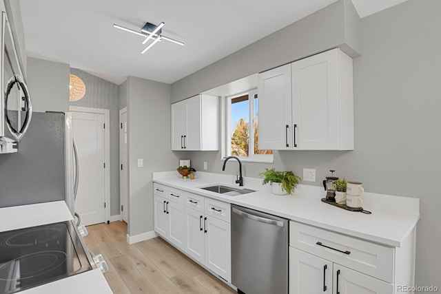 kitchen featuring light countertops, appliances with stainless steel finishes, white cabinets, a sink, and light wood-type flooring