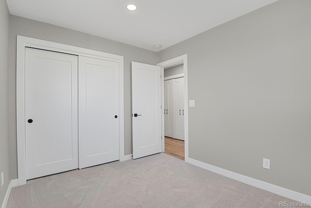 unfurnished bedroom with recessed lighting, a closet, light colored carpet, and baseboards