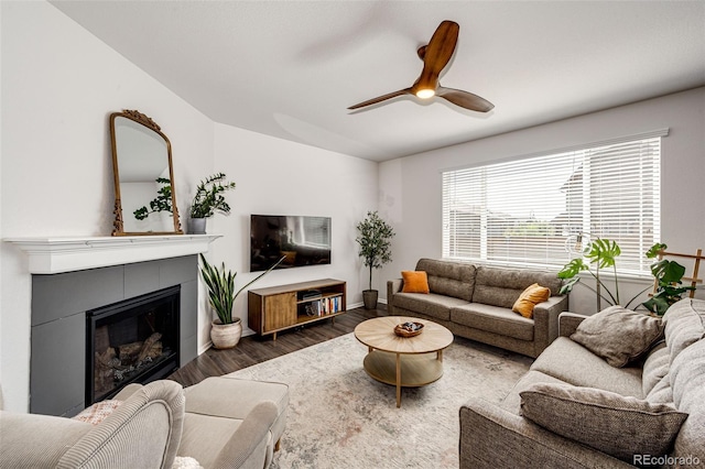 living room with a tile fireplace, ceiling fan, and dark wood-type flooring