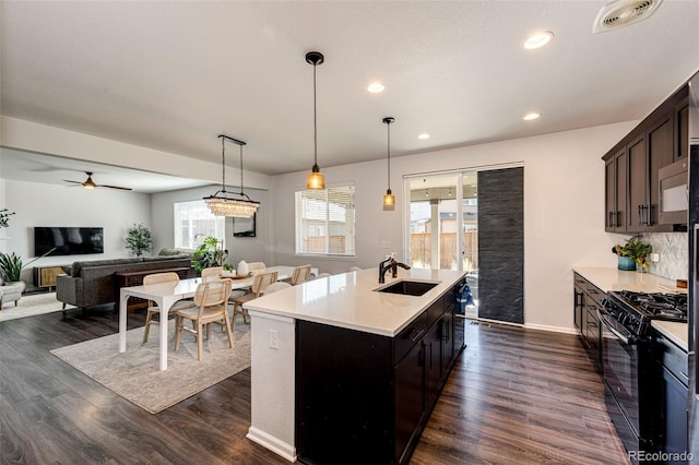 kitchen featuring ceiling fan, sink, black gas range oven, dark hardwood / wood-style flooring, and an island with sink