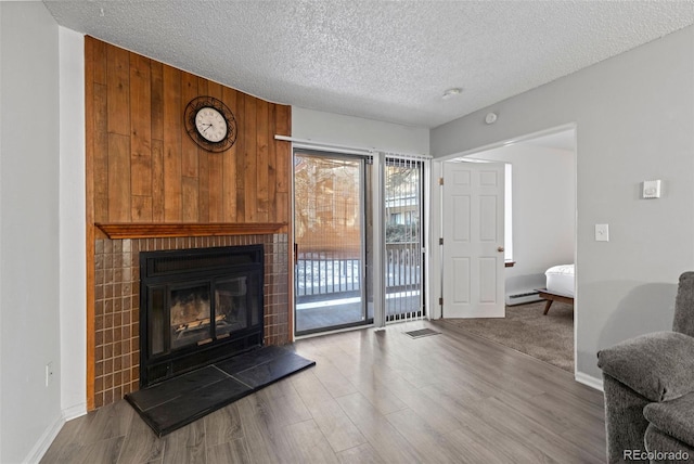 living room featuring hardwood / wood-style floors, wood walls, a baseboard heating unit, a brick fireplace, and a textured ceiling