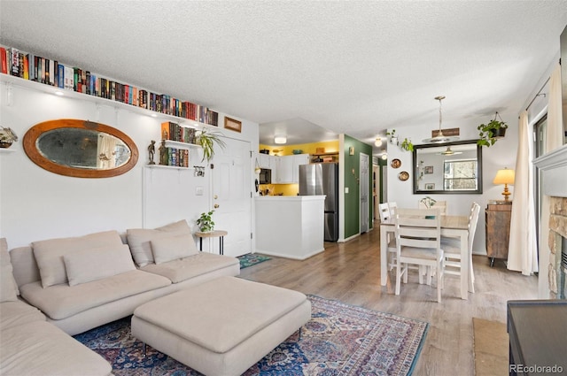 living room with ceiling fan, a textured ceiling, and light wood-type flooring