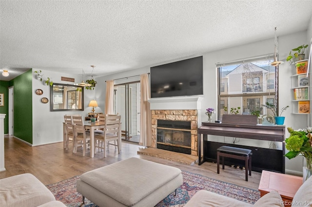 living room with a stone fireplace, wood-type flooring, and a textured ceiling