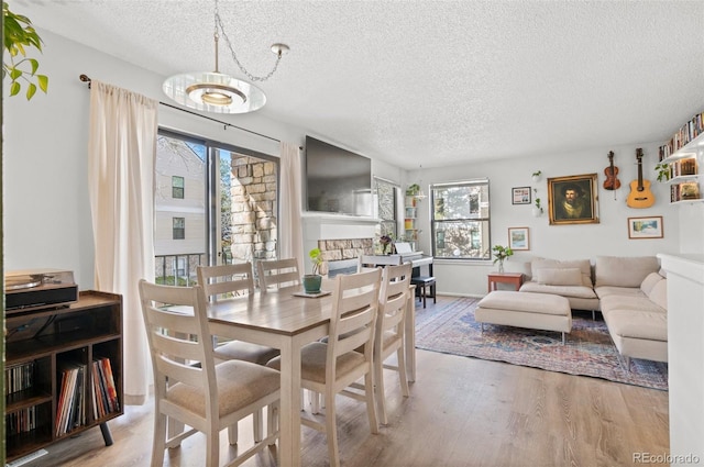 dining room with wood-type flooring, a textured ceiling, and a stone fireplace