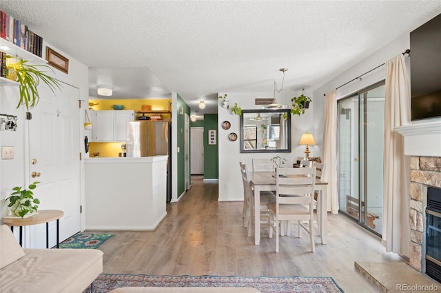 dining space featuring a stone fireplace, a textured ceiling, and light wood-type flooring