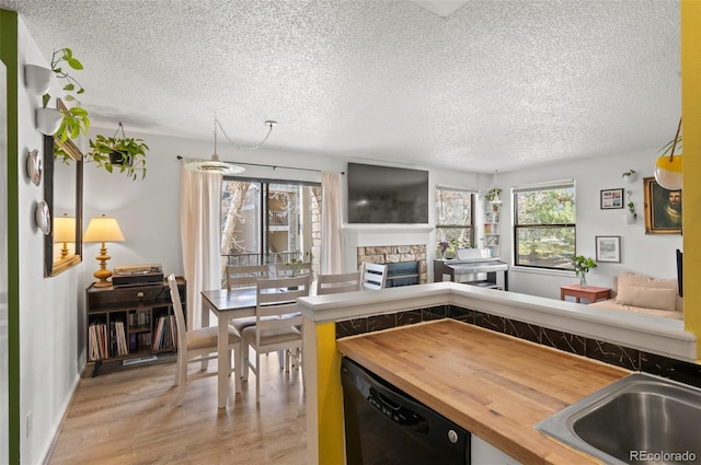 kitchen with dishwasher, sink, light wood-type flooring, a fireplace, and butcher block countertops