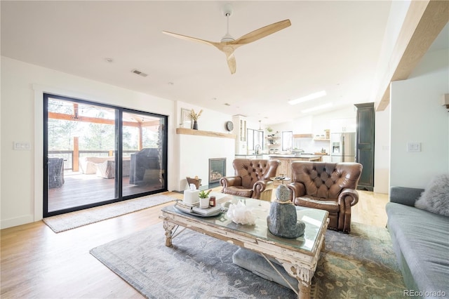 living room with visible vents, a glass covered fireplace, lofted ceiling, ceiling fan, and light wood-style floors