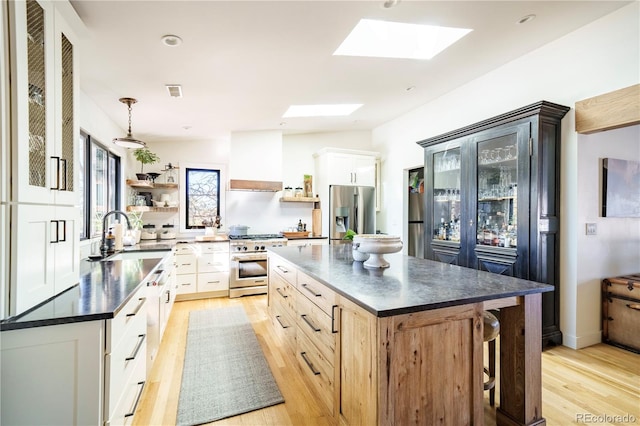 kitchen with open shelves, stainless steel appliances, dark countertops, custom range hood, and a sink