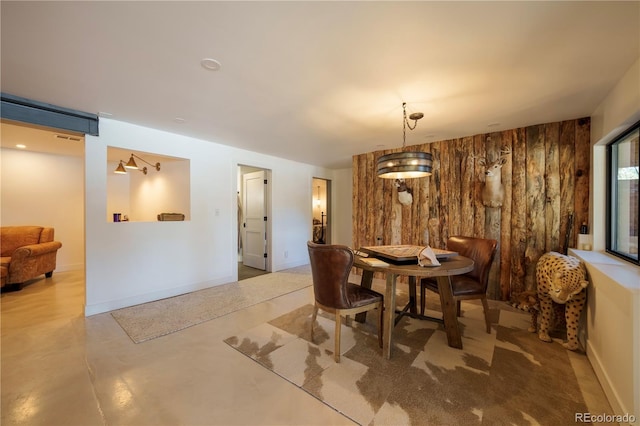 dining space featuring wood walls, concrete floors, and baseboards