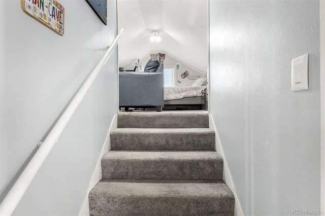 stairs featuring lofted ceiling and a textured wall