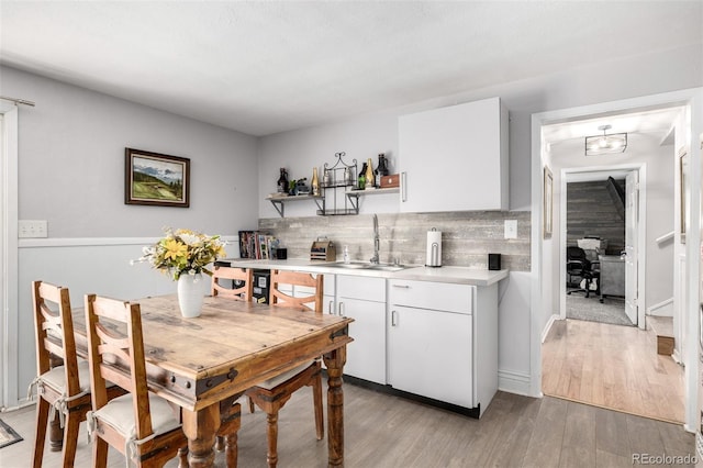 kitchen with open shelves, light countertops, decorative backsplash, light wood-style floors, and a sink