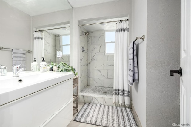 full bath featuring tiled shower, a textured wall, and vanity