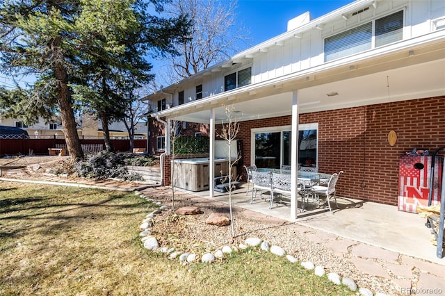 rear view of property with brick siding, fence, board and batten siding, a patio area, and a hot tub