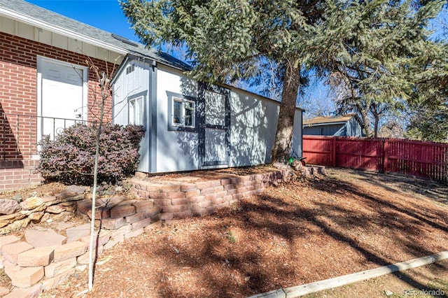 view of property exterior with brick siding, roof with shingles, and fence