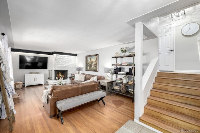 living room featuring light wood-type flooring, a fireplace, and stairs