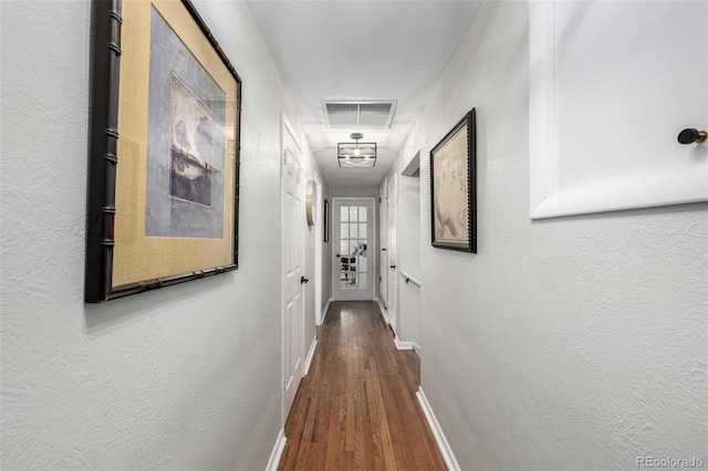 hallway with attic access, baseboards, visible vents, a textured wall, and wood finished floors