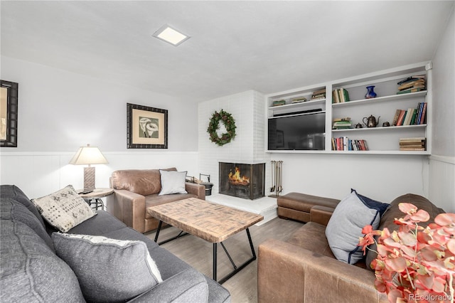 living area featuring a brick fireplace, a wainscoted wall, and wood finished floors