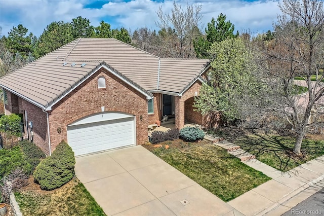 view of front facade featuring brick siding, a tile roof, an attached garage, and driveway